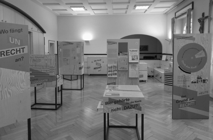 Ein Ausstellungsraum des Museums mit Schautafeln mit deutschen Texten über Recht und Demokratie, die auf Holzständern angeordnet sind. Der Boden ist aus Holz und der Raum ist mit großen Fenstern und gewölbten Türen gut beleuchtet. Ein Ausstellungsraum des Museums mit Schautafeln mit deutschen Texten über Recht und Demokratie, die auf Holzständern angeordnet sind. Der Boden ist aus Holz und der Raum ist mit großen Fenstern und gewölbten Türen gut beleuchtet.
